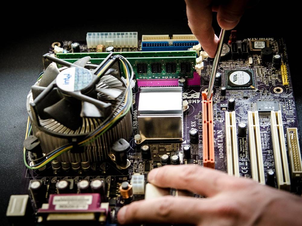 Hand mit Schraubendreher an einem ausgebauten Mainboard mit CPU-K&uuml;hler